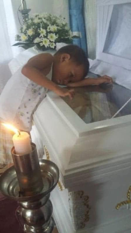 A boy hugs his mother’s coffin.